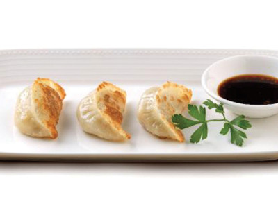Three gyoza dumplings on rectangular serving dish with soya dipping sauce.