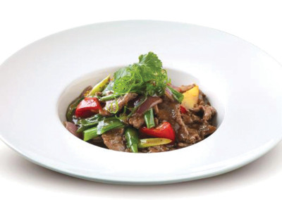 Mango beef with vegetables on a round white plate.